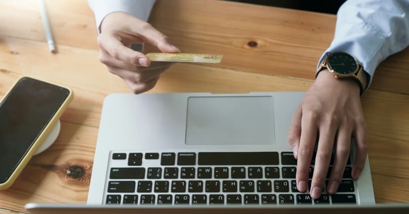 Hands with a credit card and laptop on a wooden desk, symbolizing payment and digital billing in the AI era